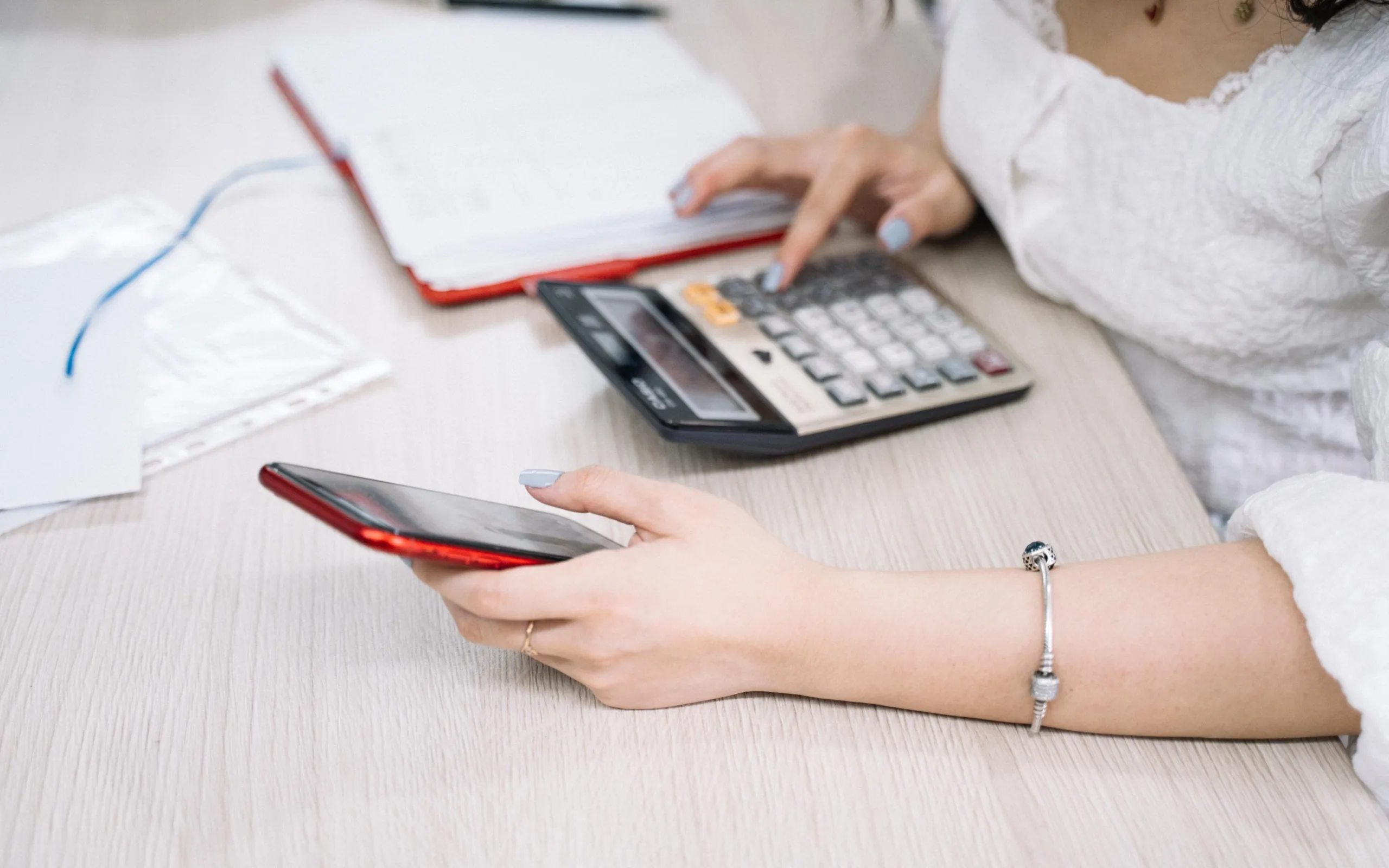 Une porteuse de projet calcule ses charges sociales à son bureau, calculatrice et smartphone à portée de main
